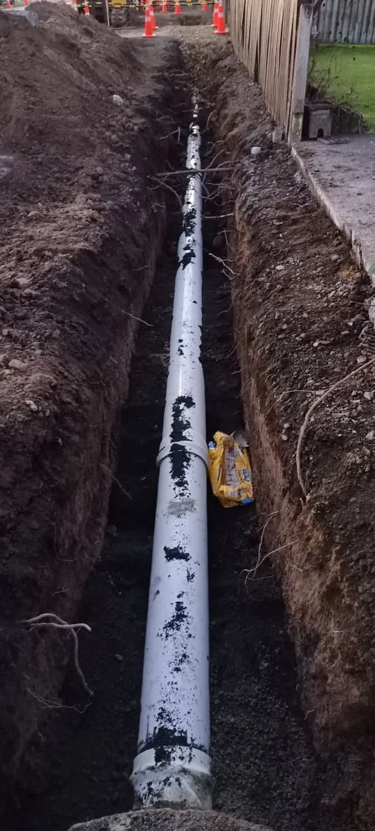 New drainage pipe being installed and bedded in a trench on an Auckland building site, excavator and gravel base visible