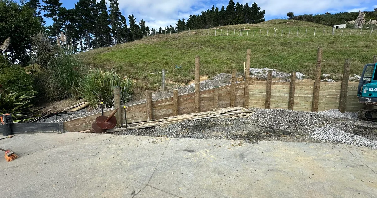 Retaining wall under construction on a sloped Auckland section, drainage aggregate visible behind blocks before backfill
