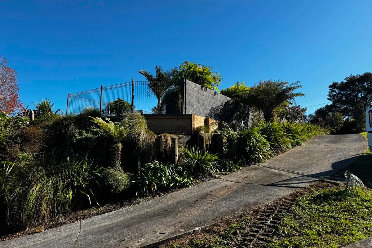 Retaining wall alongside a driveway on a sloped Auckland property, showing how vehicle access above the wall adds surcharge load