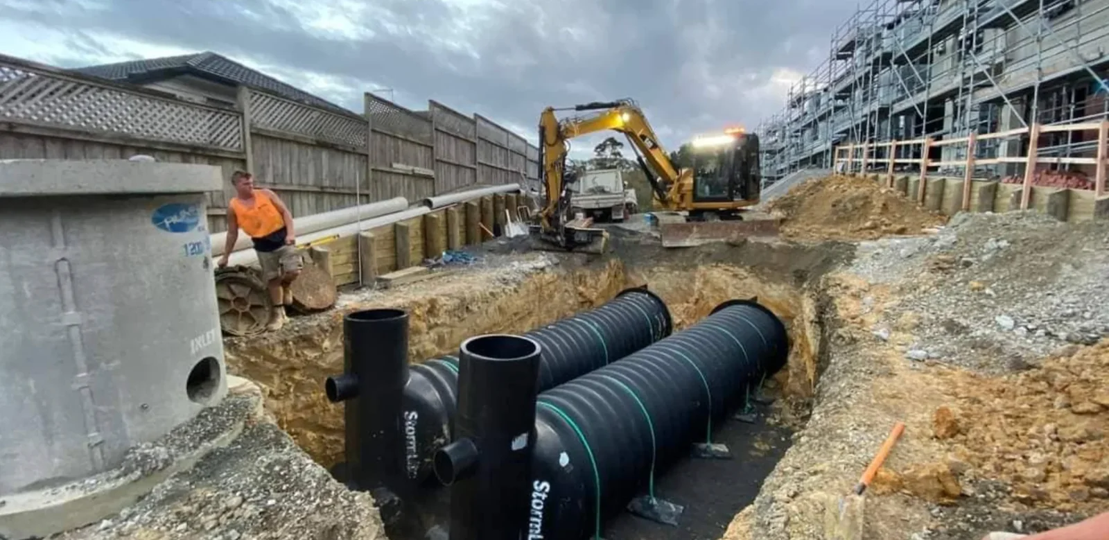 A stormwater detention tank sitting in an open trench on an Auckland clay site, surrounded by drainage gravel and connected pipework before backfilling