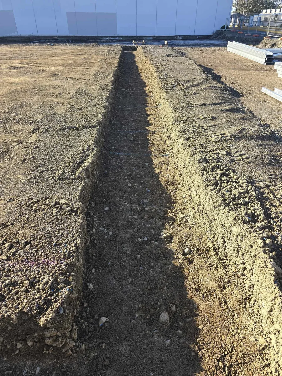 Excavated subsoil drainage trench on a wet Auckland section, with standing water visible in the surrounding saturated clay ground