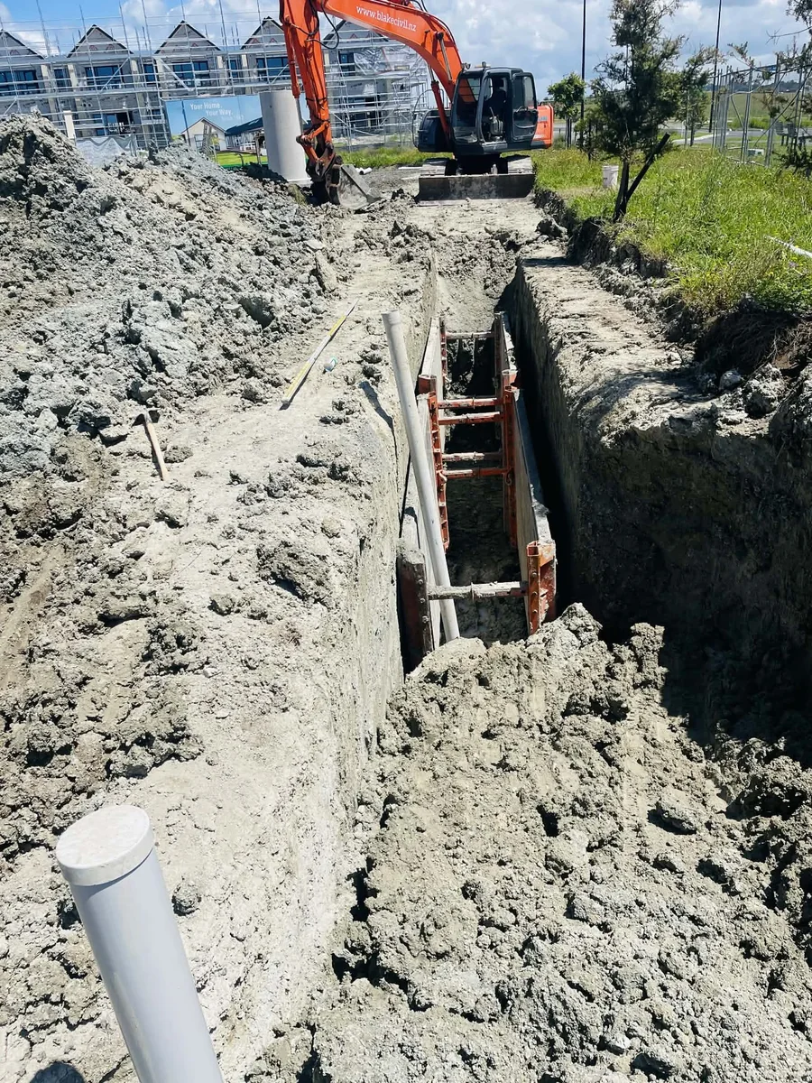 A subsoil drainage trench on an Auckland section showing perforated pipe laid in the base surrounded by drainage metal, with filter cloth lining the trench