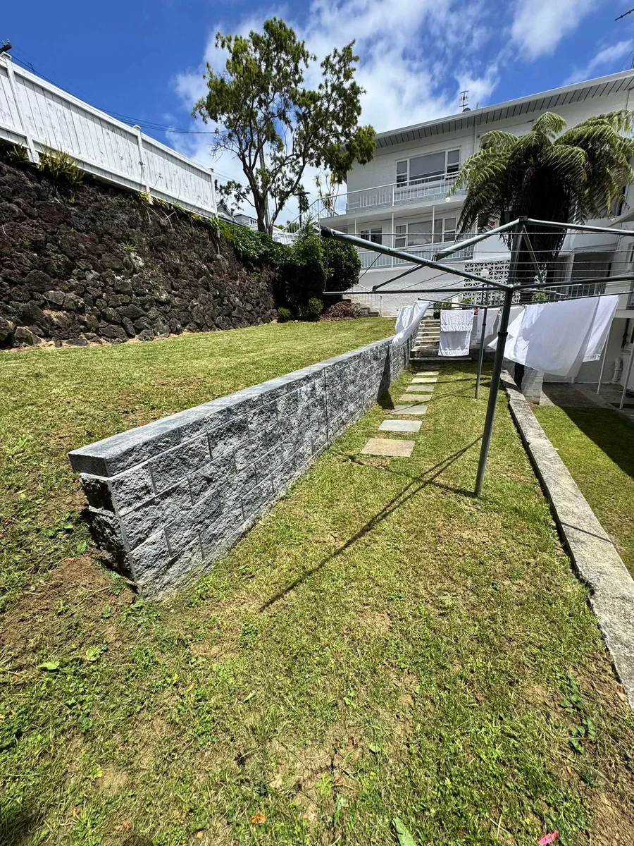 A finished keystone block retaining wall curving along a landscaped Auckland residential section